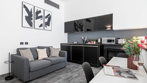 Un espace de vie moderne comprenant un canapé gris, une table à manger et un coin cuisine équipé d’un four à micro-ondes.