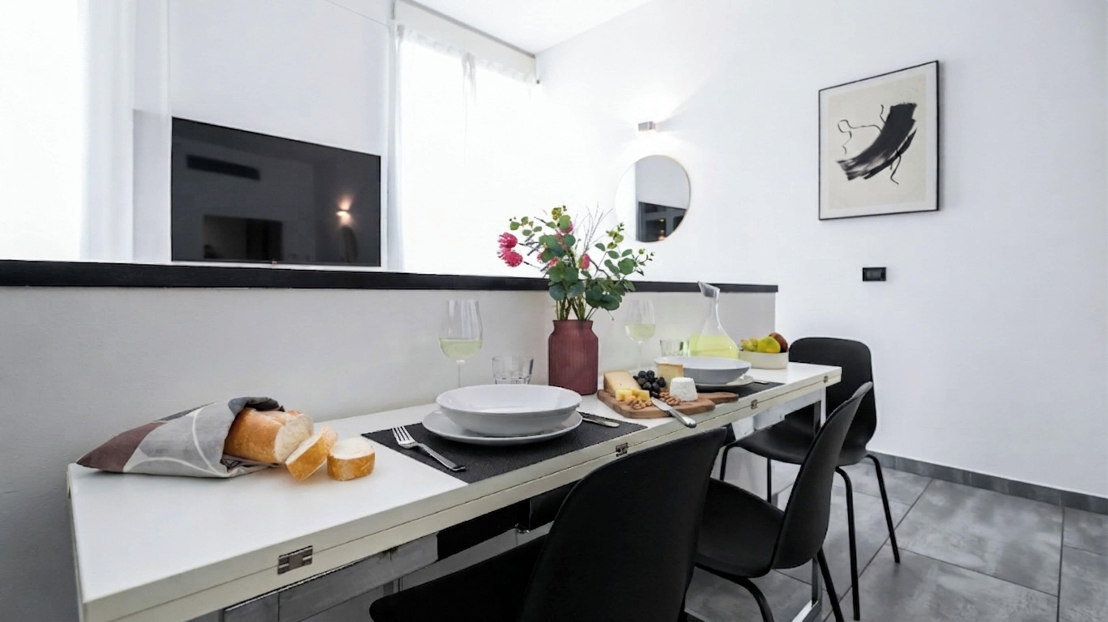 A modern dining area with a white table, black chairs, and a vase of flowers.
