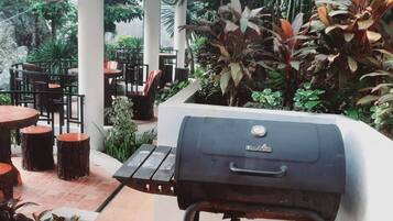 Eine Terrasse im Freien mit Holzkohlegrill, runden Tischen und Stühlen.