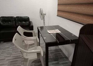 A room with a black leather sofa, a small table with a fan, and a white plastic chair. - Avana Hills Boracay Prime Residence (Boracay Island)