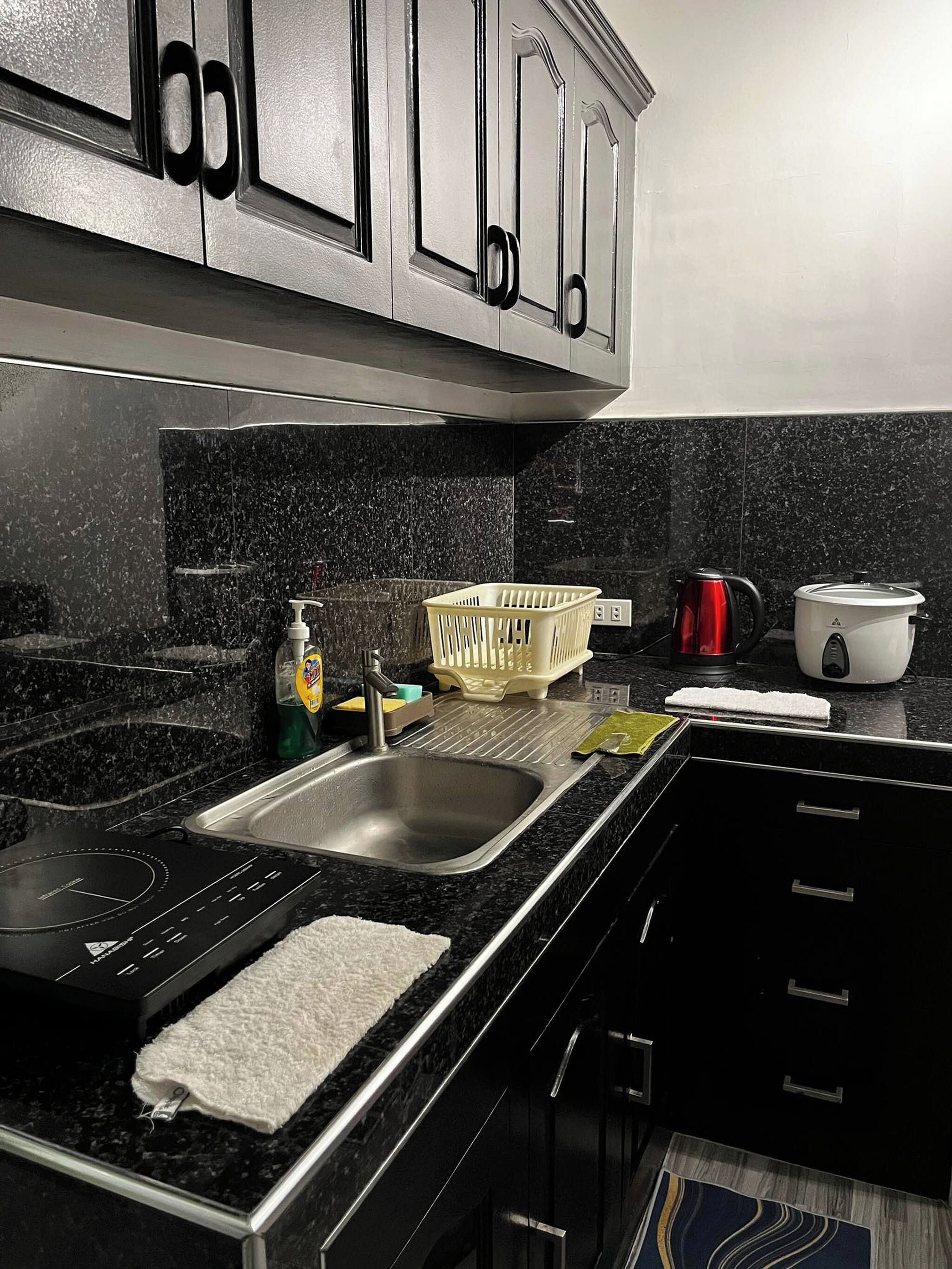 A kitchen with a stainless steel sink, a kettle, a dish rack, and a stove.
