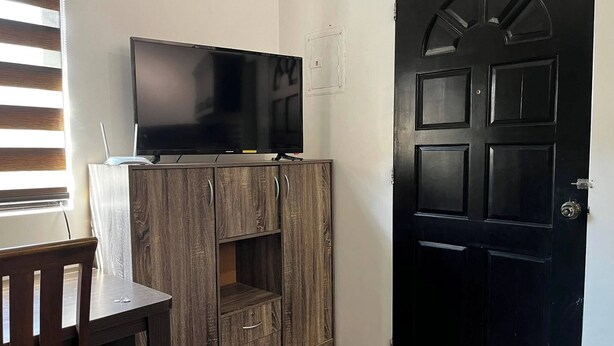 Une pièce avec un téléviseur posé sur un meuble en bois, une porte et une fenêtre avec des stores.
