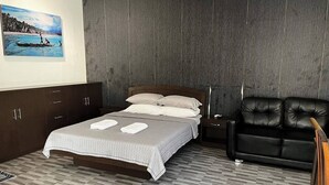 Une chambre à coucher avec un lit, un fauteuil en cuir noir, une armoire en bois et un tableau accroché au mur.