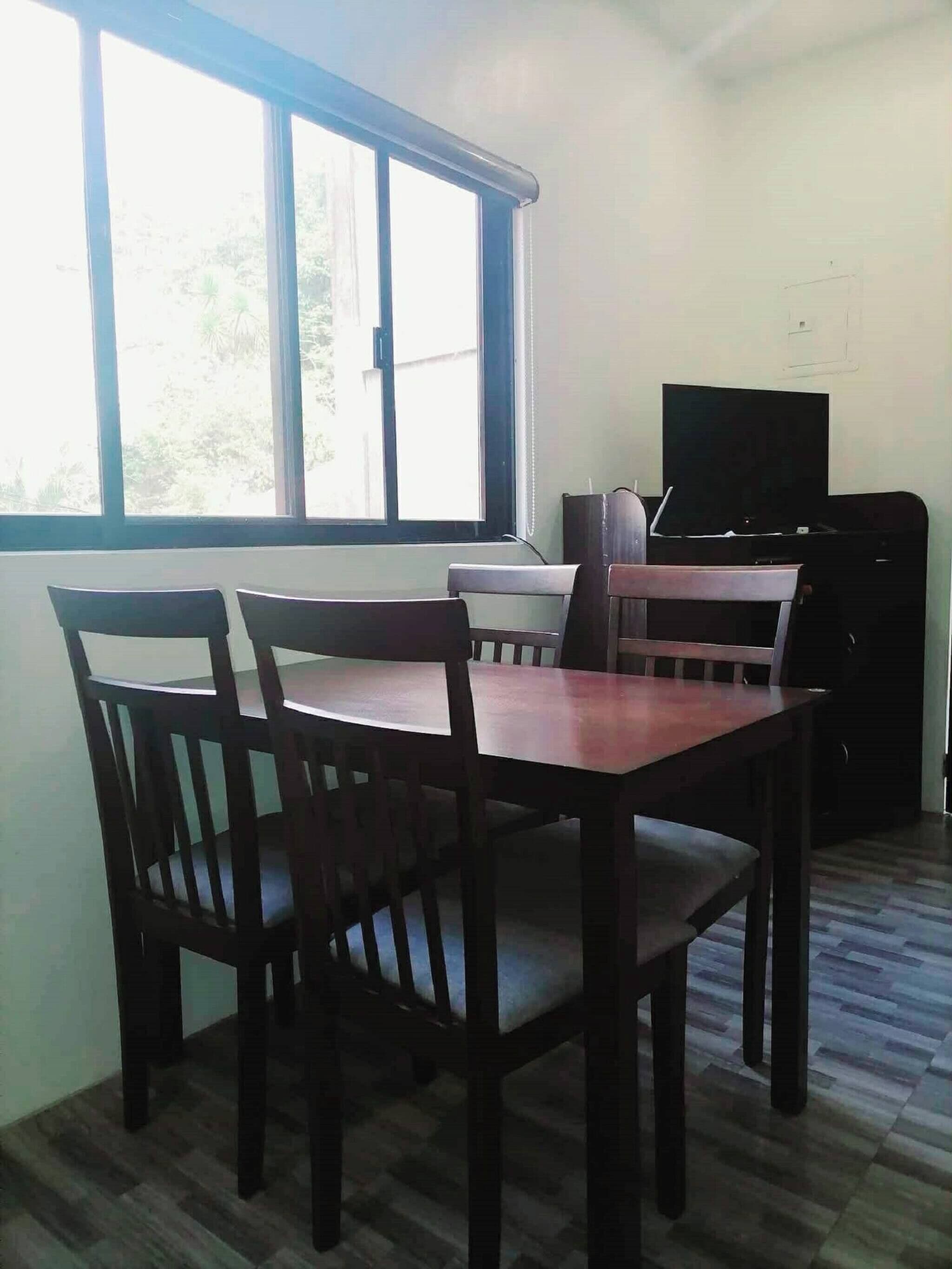 Una habitación con una mesa de comedor y sillas, un televisor y una ventana con vista a follaje.