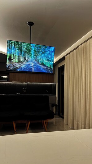 En moderne stue med et stort fladskærms TV på væggen, en mørk lædersofa og et vindue med gardiner.