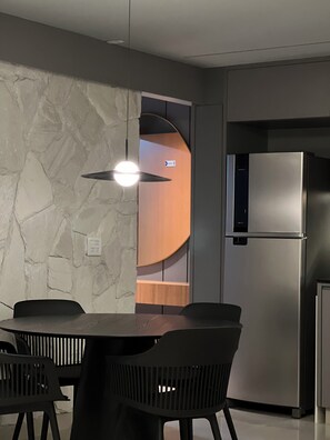 A modern kitchen with a built-in refrigerator, a dining table with chairs, and a stone-textured wall. - Fully equipped apartment •  Excellent location with garage. (Goiânia)