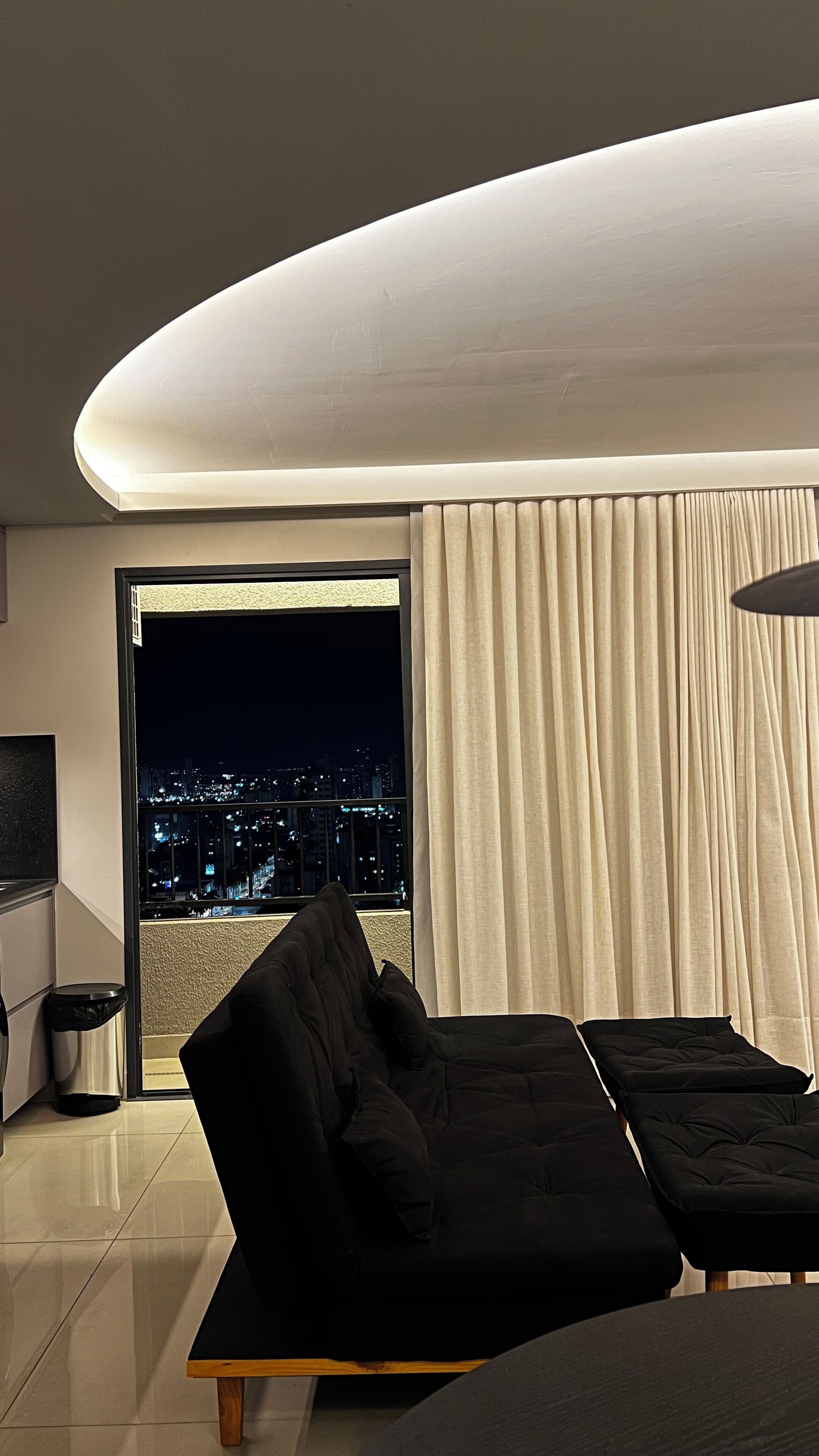 Ein modernes Schlafzimmer mit Stadtblick, einem schwarzen Sofa und einer Deckenleuchte mit gebogenem Lampenschirm.