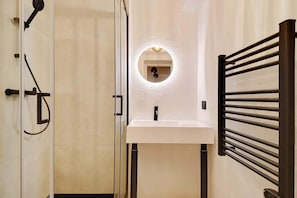 Ein Badezimmer mit Glastür, Waschbecken in Weiß, rundem Spiegel und Handtuchhalter.