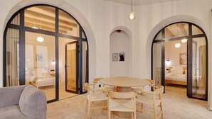 A hotel room with a round wooden table, multiple chairs, a sofa, and large arched windows. - A Authentic 3-BR/2Ba in Opera - Grands Boulevards (Paris)