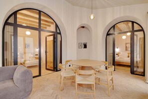 A hotel room with a round wooden table, multiple chairs, a sofa, and large arched windows. - A Authentic 3-BR/2Ba in Opera - Grands Boulevards (Paris)