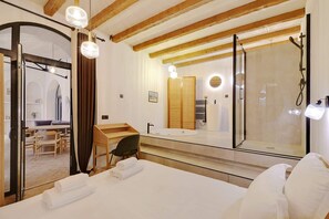 Hotellihuone, jossa on sänky, työpöytä, tuoli, peili ja suihkutila.