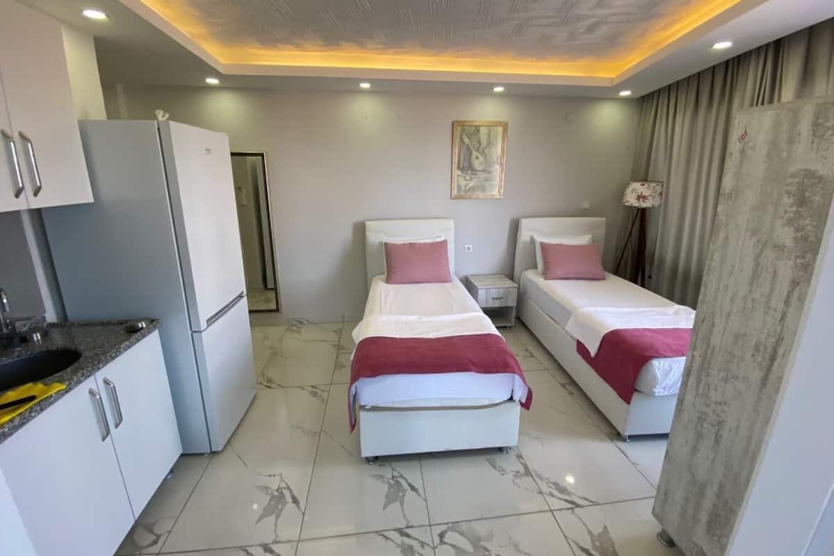 Une chambre d’hôtel de taille réduite, comprenant deux lits simples, une kitchenette et une salle de bain.