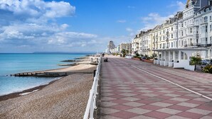 A seaside promenade with a pebble beach, a promenade with red and grey tiles, and white terraced houses.