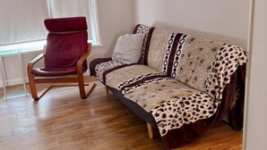 A living room with a wooden floor, a red chair, a patterned sofa, and a painting on the wall.