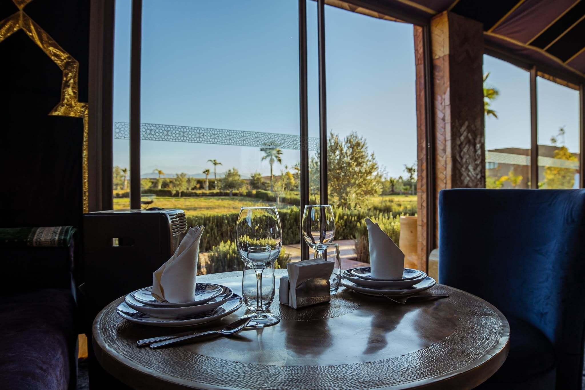 Une table dressée pour deux personnes, avec vue sur un jardin aménagé, grâce à de grandes fenêtres.