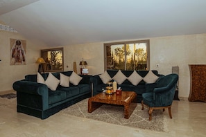 Ein Wohnzimmer mit zwei dunkelgr ünen Sofas, gemusterten Kissen, einem Holztisch und Blick auf Bäume durch große Fenster.