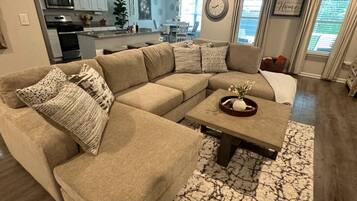 Ein Wohnzimmer mit einem Ecksofa, einem Couchtisch und einem gemusterten Teppich.