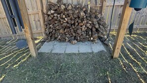 Una estructura de madera con una pila de leña debajo.