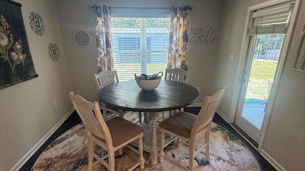 Un comedor con una mesa redonda, cuatro sillas, una alfombra y un ventanal con cortinas.