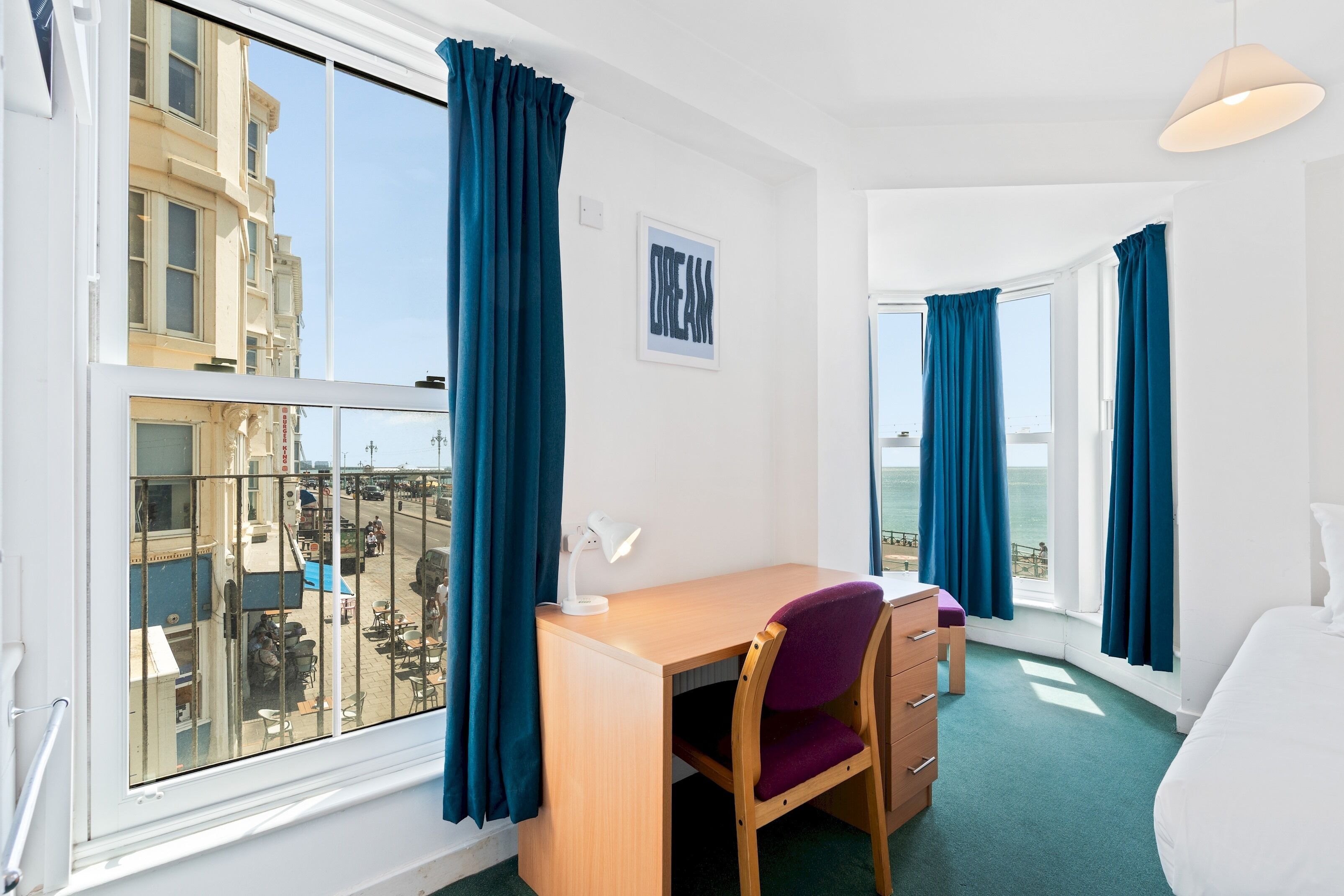 A room with a desk, chair, and a view of the sea through large windows.