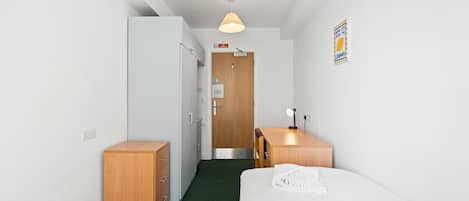 A hotel room with a bed, a desk with a lamp, a wardrobe, a door, and a wall-mounted sign.