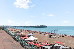 A beach with umbrellas, lounge chairs, and a pier in the background. - Kings Residence 2 | By My Getaways (Brighton)