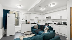 Eine moderne Küche mit weißen Schränken, einem blaugrünen Sofa und einem kleinen runden Tisch.