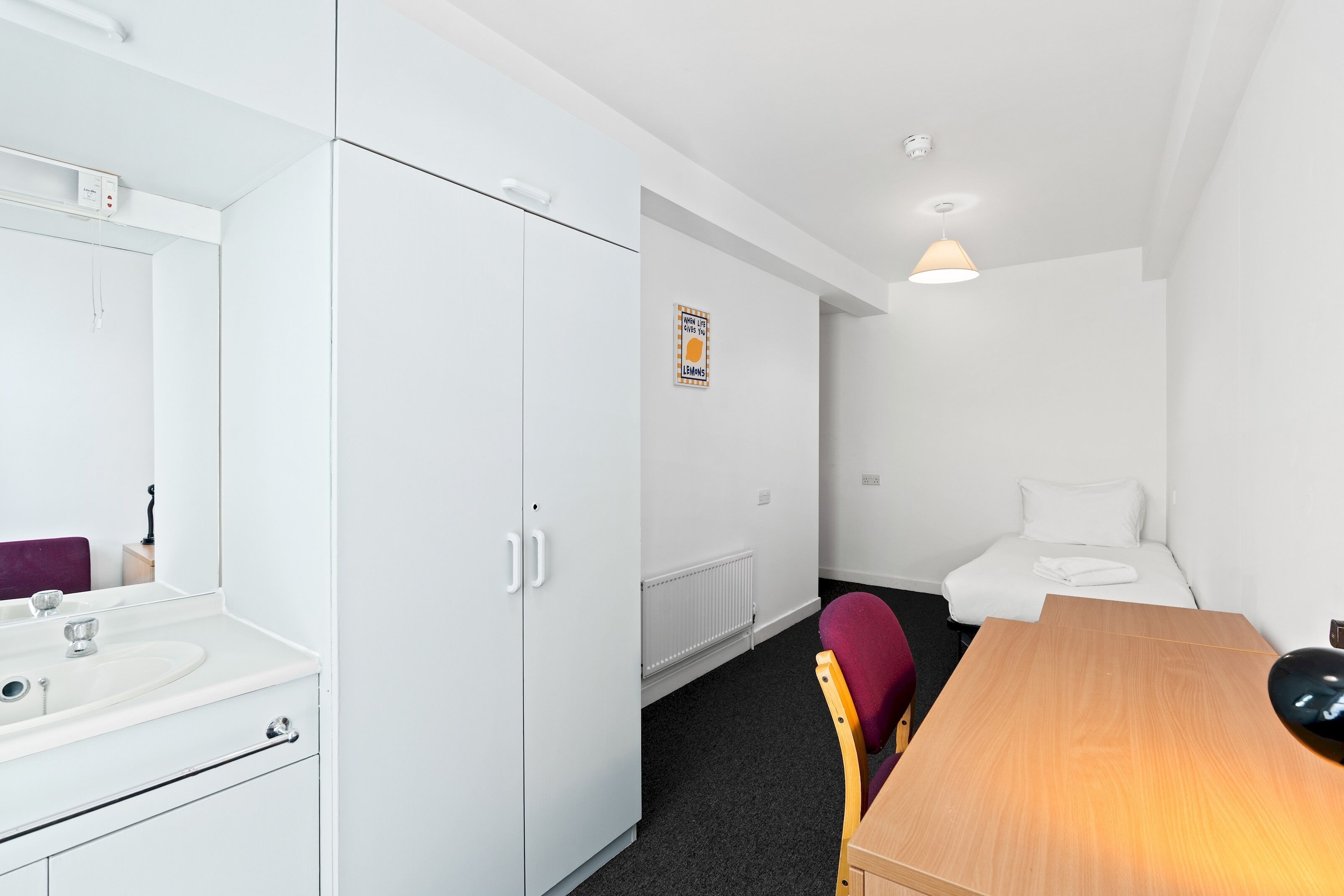Ein Hotelzimmer mit Bett, Schreibtisch, Stuhl, Badezimmer mit Spiegel und Heizkörper.