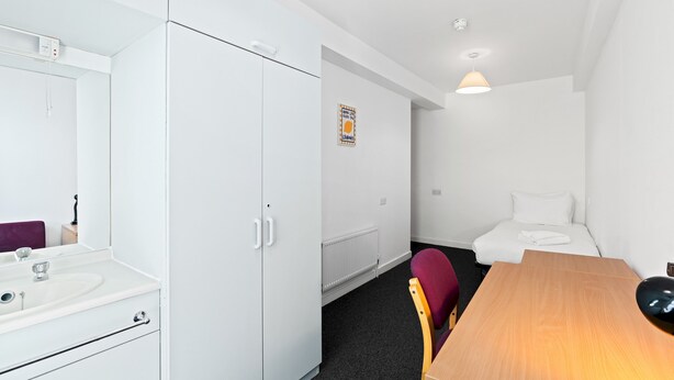 Ein Hotelzimmer mit Bett, Schreibtisch, Stuhl, Badezimmer mit Spiegel und Heizkörper.