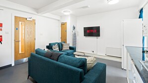 Ein modernes Wohnzimmer mit Türkis-Sofas, einem Flachbildfernseher und einem kleinen runden Tisch.