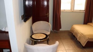 Habitació petita amb un llit, una cadira, una taula petita i una porta.
