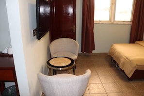 A small room with a bed, a chair, a small table, and a door.