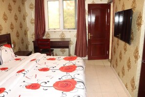 A bedroom with a bed, a desk, a wardrobe, a television, and a window with curtains. - HH Inn (Lagos)