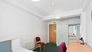 A hotel room with a bed, a desk, a chair, a radiator, a door, and a mirror. - Kings Residence 5 | By My Getaways (Brighton)