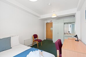 Ein Hotelzimmer mit Bett, Schreibtisch, Stuhl, Heizkörper, Tür und Spiegel.
