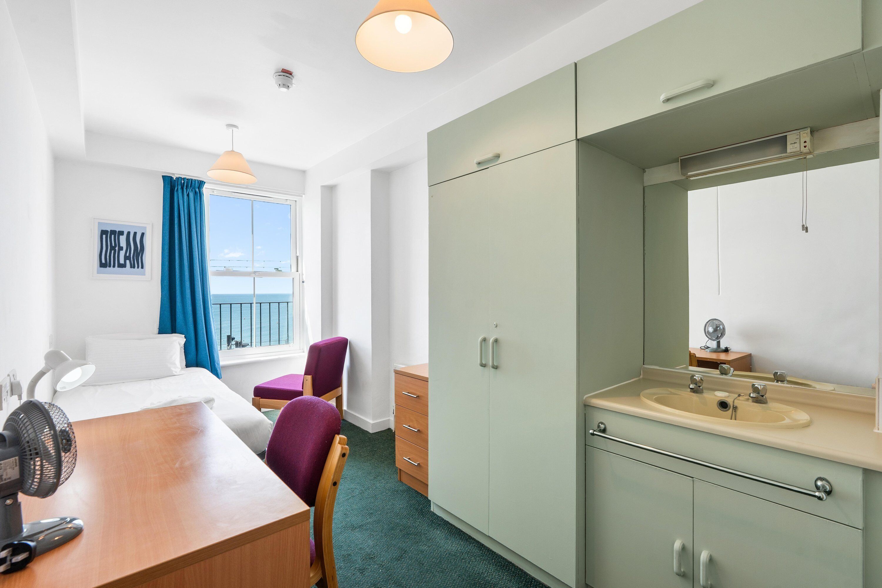 A hotel room with a bed, a desk, a chair, a wardrobe, a bathroom with a sink and mirror, and a window with a view.