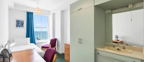 A hotel room with a bed, a desk, a chair, a wardrobe, a bathroom with a sink and mirror, and a window with a view.