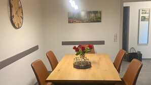 A dining area with a wooden table, six chairs, a clock, a painting, and a vase with red flowers. - Apartment Fein with Wi-Fi in the Heart of the Harz (Bad Sachsa)