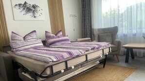 A bed with a metal frame and a woven rug, a chair, a table, and a window with curtains. - Apartment Fein with Wi-Fi in the Heart of the Harz (Bad Sachsa)