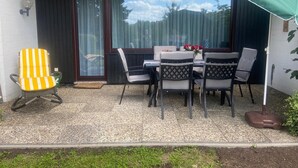 Eine Terrasse mit Tisch und Stühlen, ein gelb gestreifter Stuhl und ein grüner Sonnenschirm.