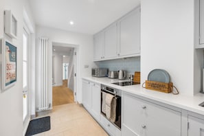 A modern kitchen with white cabinets, a built-in oven, and a microwave. - Bloomsbury Snug | By My Getaways (Brighton)