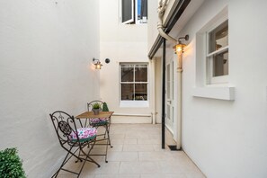 A narrow outdoor corridor with a table and chairs, a potted plant, and a window with a view. - Bloomsbury Snug | By My Getaways (Brighton)