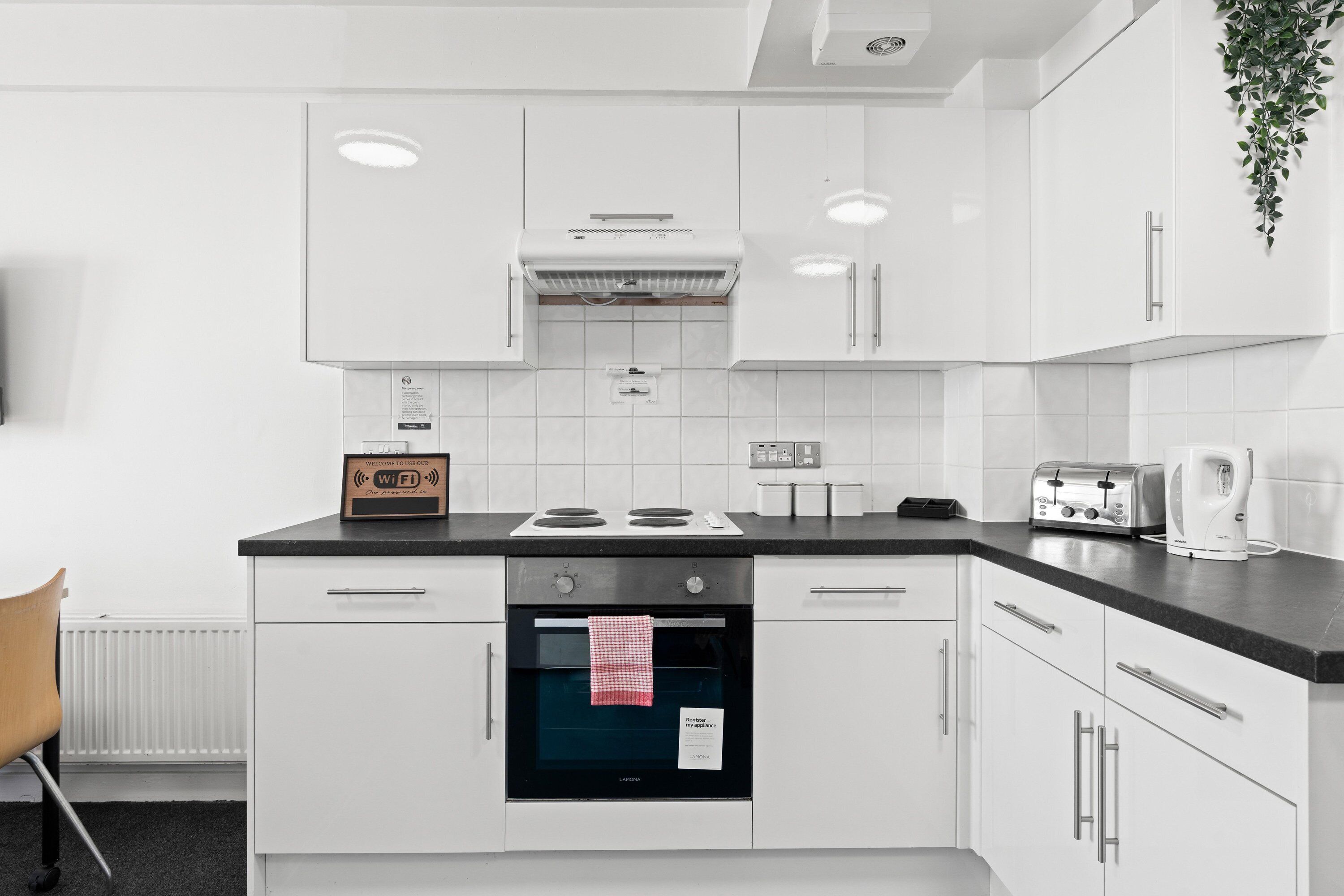 A modern kitchen with white cabinetry, a built-in oven, a stove, and a coffee maker.
