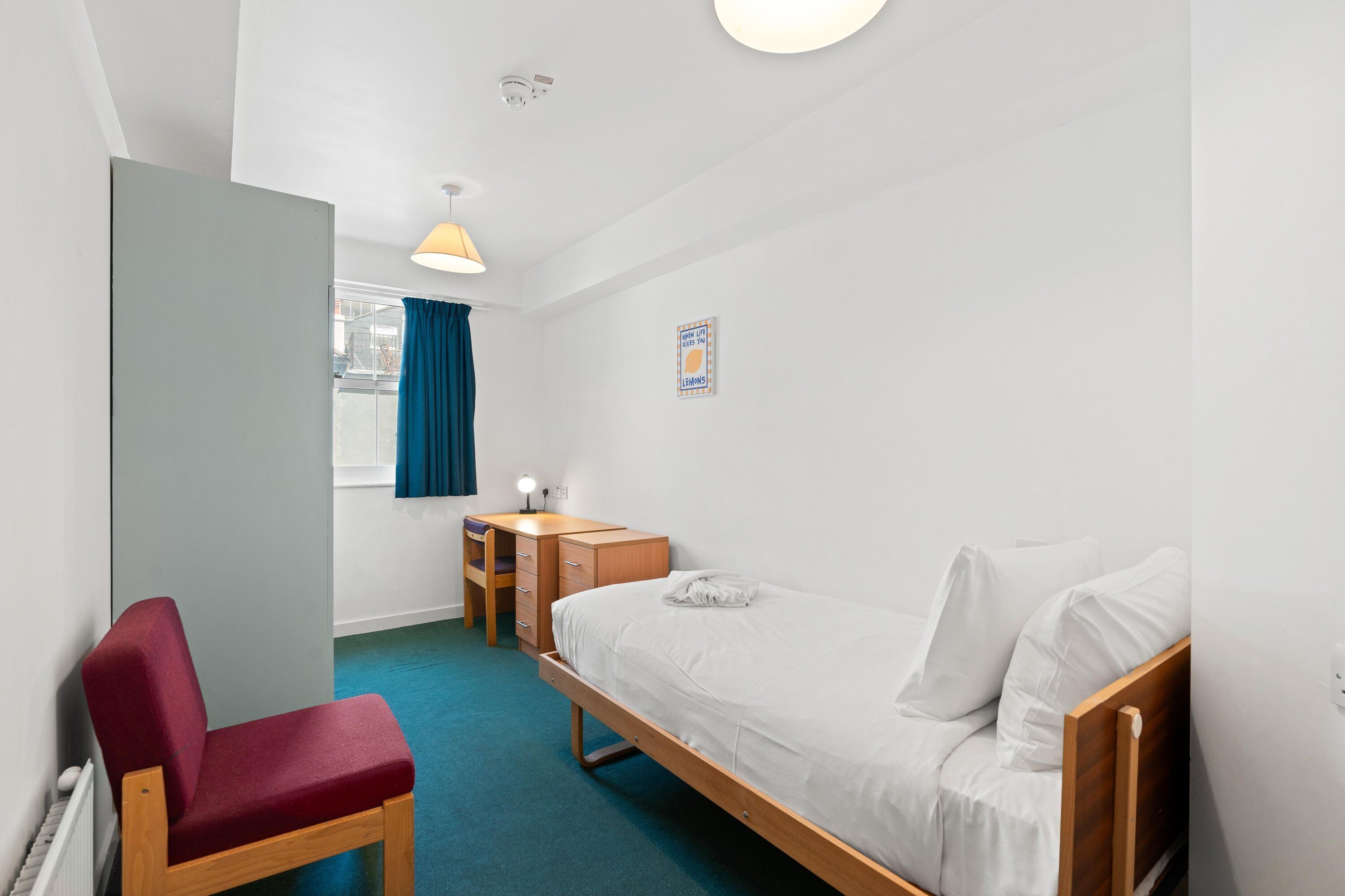 A single-bed room with a desk, chair, and a window with curtains.