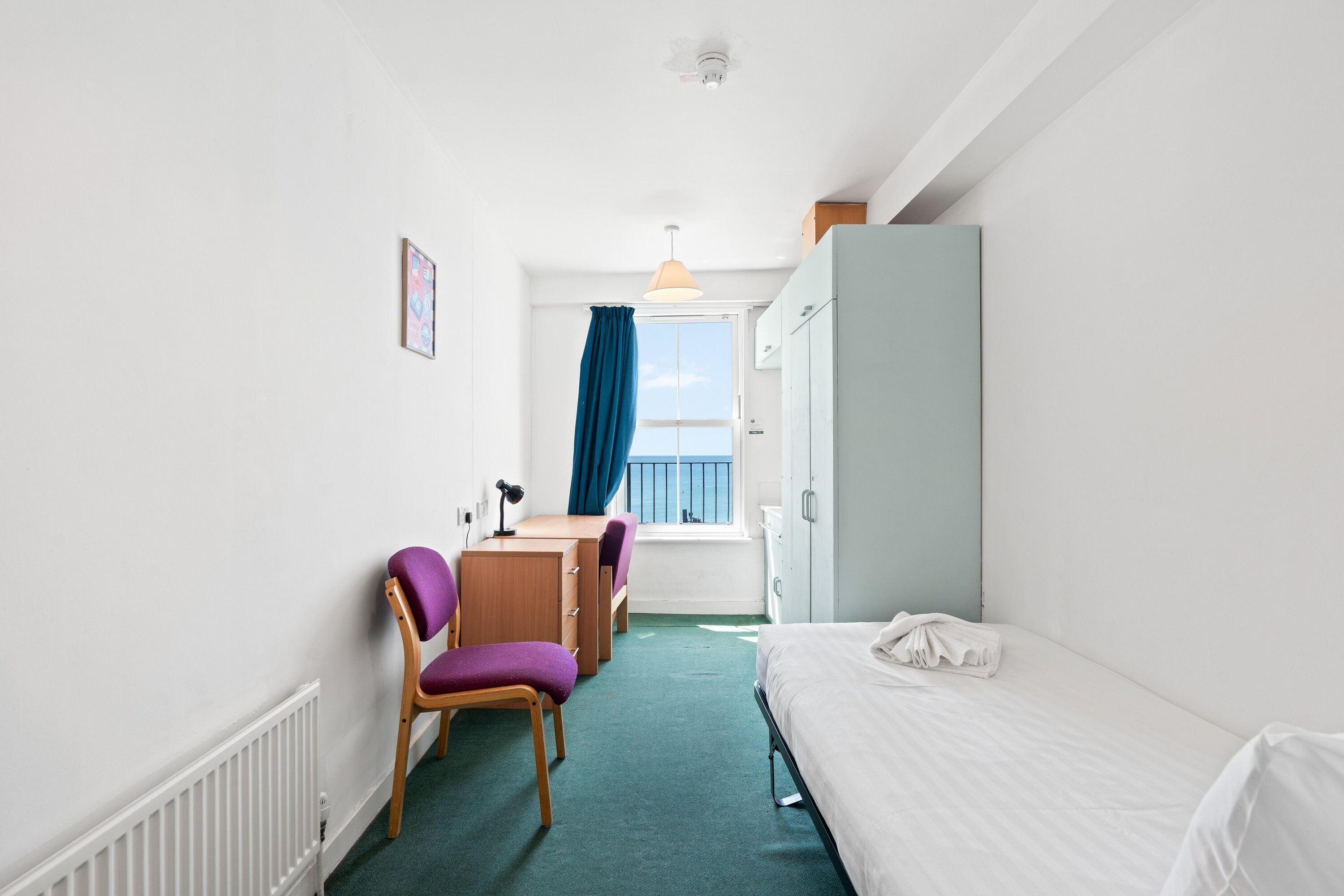 Ein Hotelzimmer mit Bett, Schreibtisch, Stuhl, einem Fenster mit Ausblick und einer Heizung.