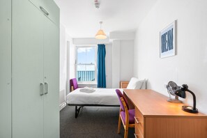 A hotel room with a bed, a desk, a chair, a window with a view, and a ceiling-mounted light fixture. - Kings Residence 9 | By My Getaways (Brighton)