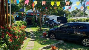 A paved pathway leading to a building with colorful flags, a parked car, and a garden with red flowers. - Charming 2-bedroom house with AC in vibrant Salvador (Salvador)