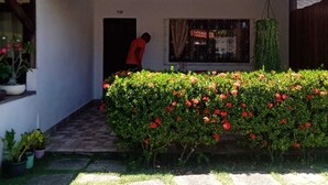 A two-story building with a balcony, a small garden with red flowers, and a person standing in the doorway. - Charming 2-bedroom house with AC in vibrant Salvador (Salvador)