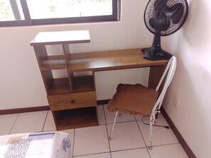 A room with a wooden desk, a chair, a standing fan, and a window. - Charming 2-bedroom house with AC in vibrant Salvador (Salvador)