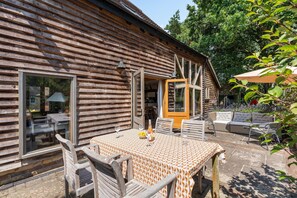 A wooden cabin with a dining area featuring a table and chairs, a covered patio, and a view of the surrounding forest. - Medleys Barn | By My Getaways (High Hurstwood)